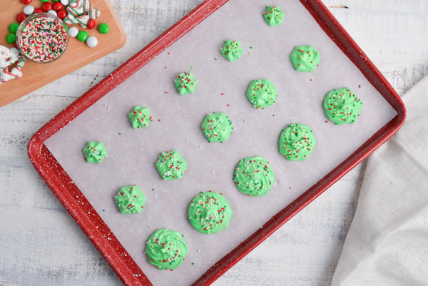 three sizes of meringue rosettes with sprinkles on a parchment lined baking tray