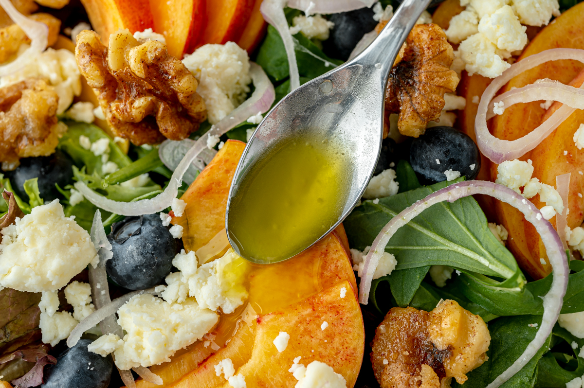 spoon adding dressing to peach salad