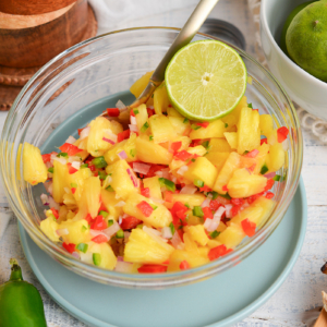 angled shot of pineapple salsa in bowl with spoon and lime