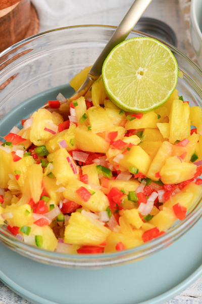 angled shot of pineapple salsa in bowl with spoon and lime