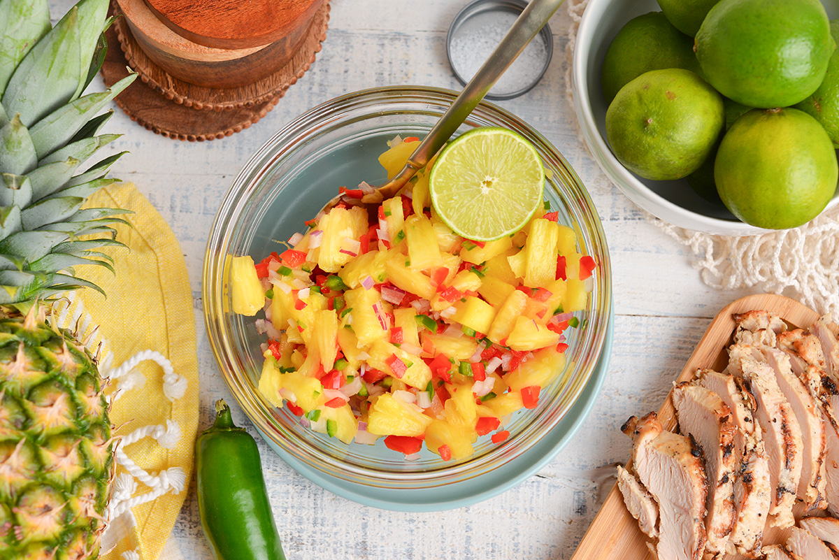 overhead shot of bowl of pineapple salsa with spoon and lime