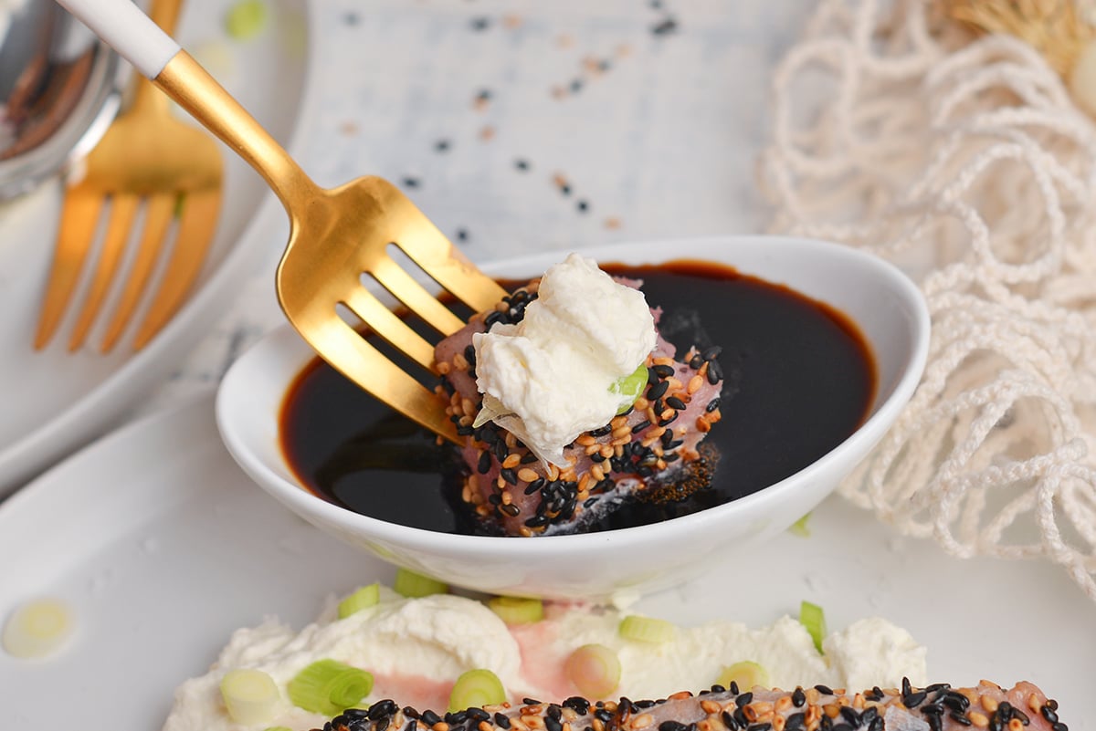 bite of sesame crusted tuna dipping into sauce on fork