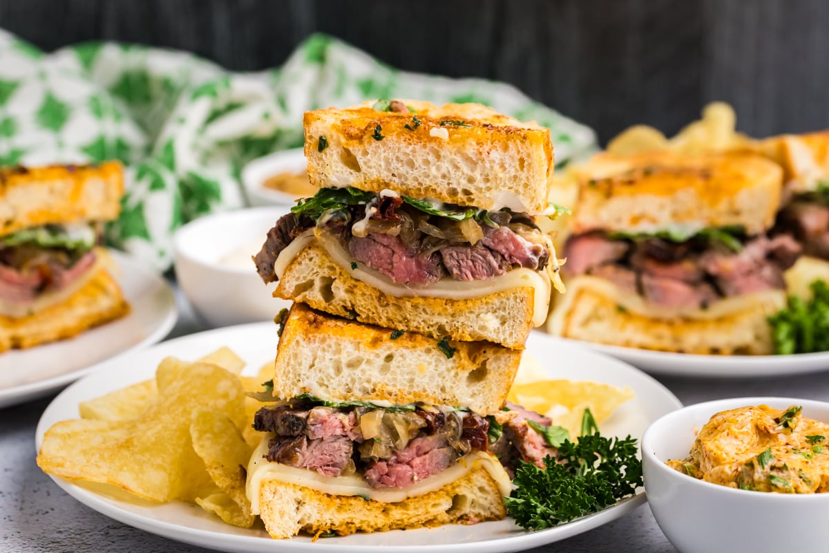 stack of two steak sandwiches on plate with chips