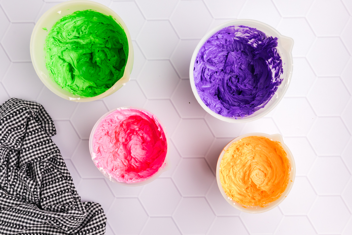 green, purple, pink and orange frosting in bowls