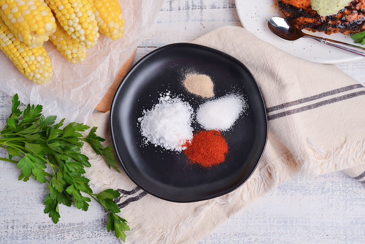 overhead shot of corn on the cob seasoning ingredients on black plate