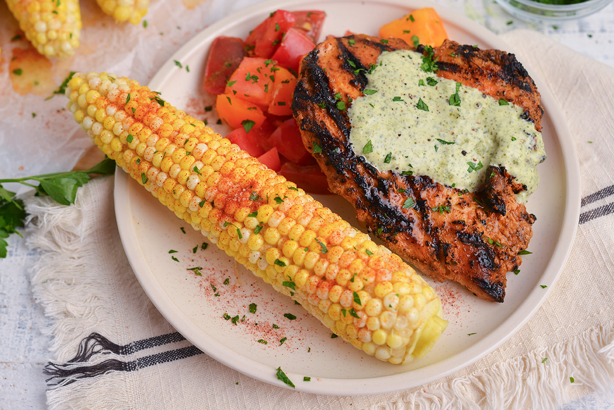 seasoned corn on the cob on plate with chicken and tomatoes