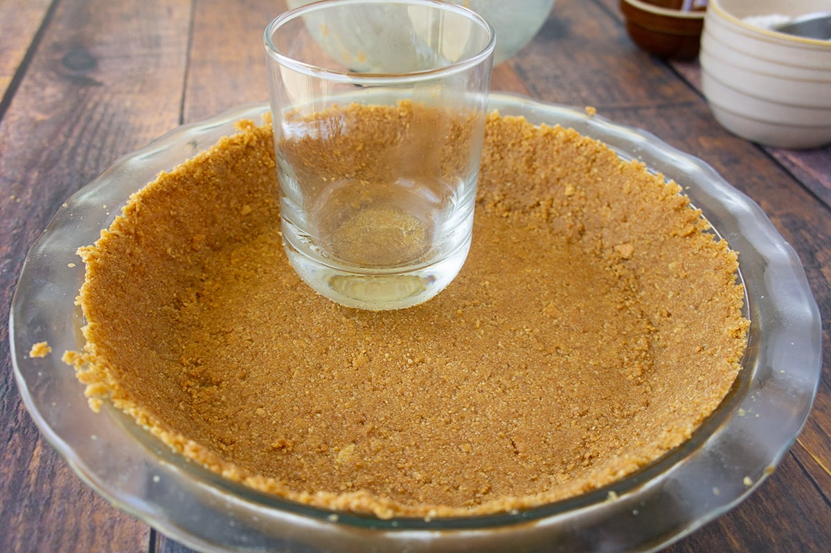 glass pressing graham crack crust into pie plate