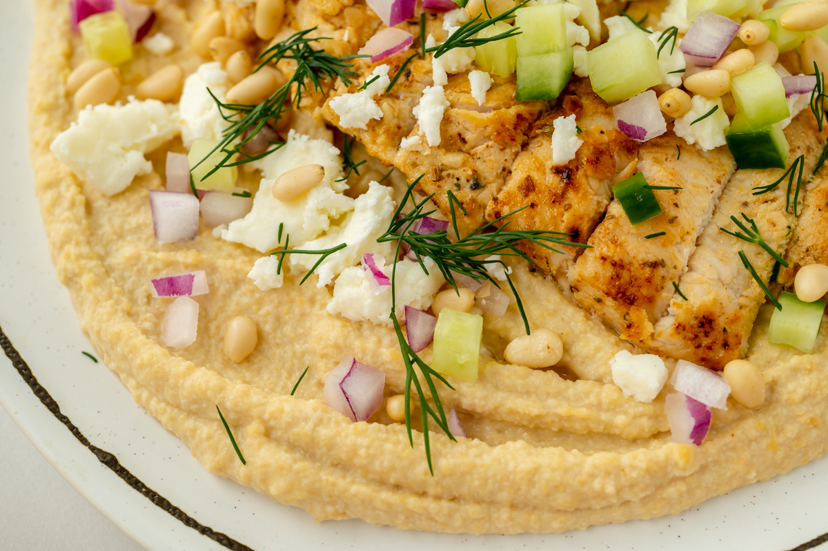 close up angled shot of hummus bowl topped with chicken and veggies