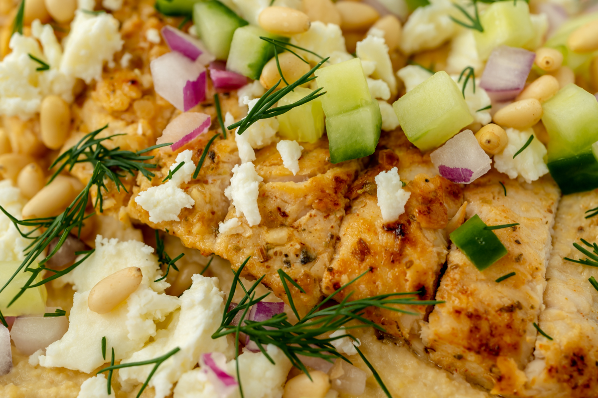 close up shot of sliced chicken on hummus bowl