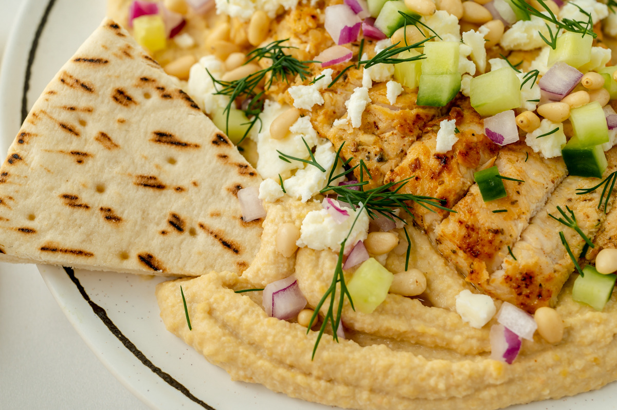 pita bread dipping into greek chicken hummus bowl