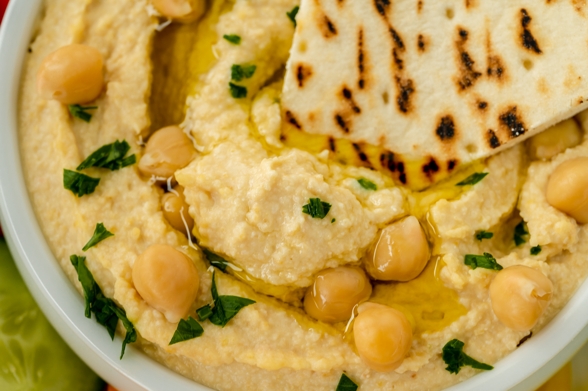 close up shot of pita dipping into bowl of homemade hummus