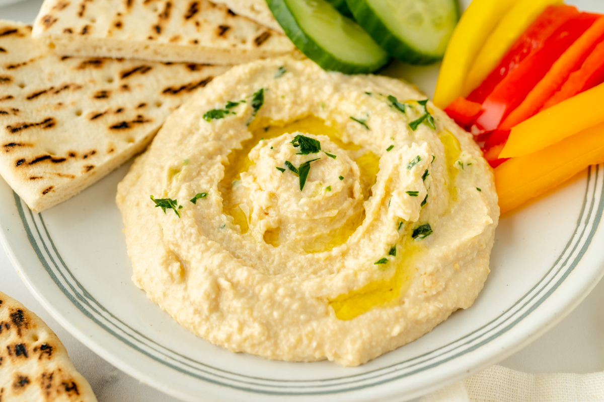 angled shot of hummus on plate with veggies and pita