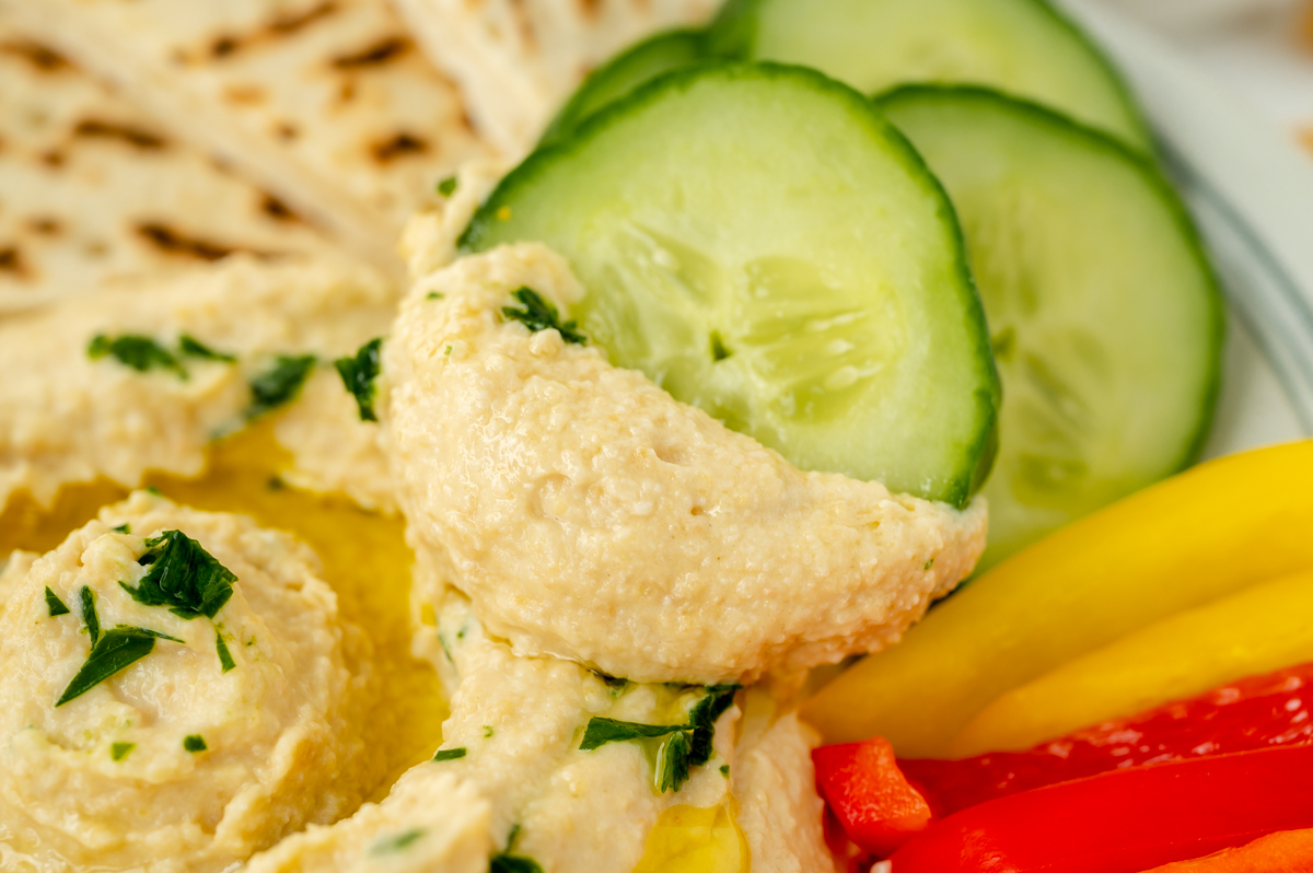 close up of cucumber slice dipped into hummus