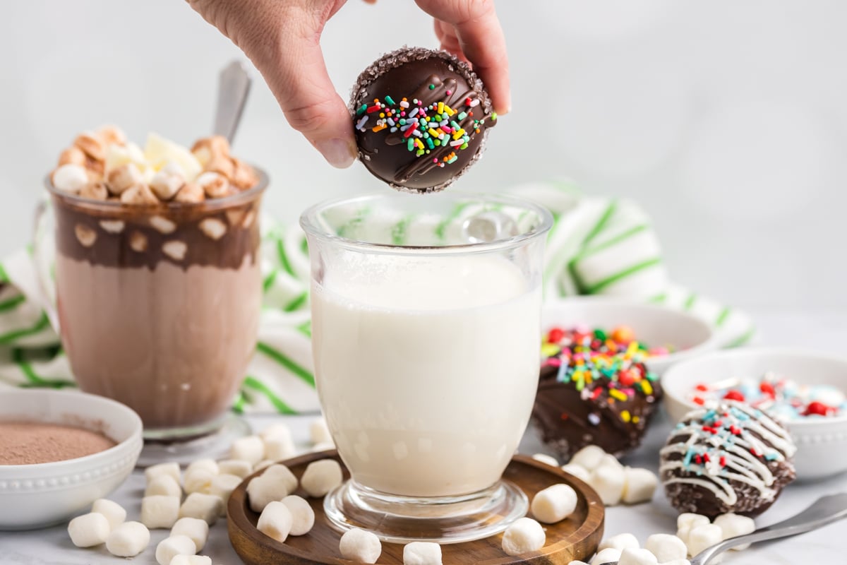 hand dropping hot chocolate bomb into hot mug of milk