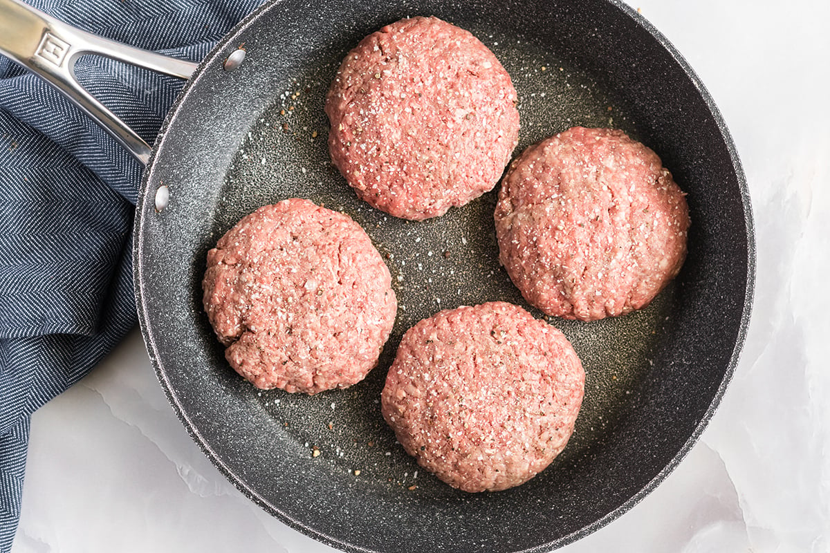 four burger patties coking in pan