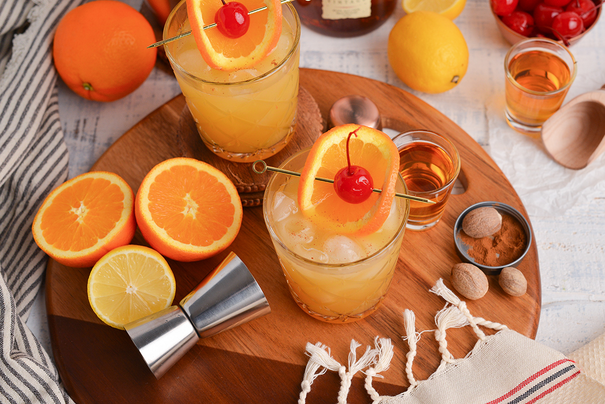 angled shot of two maple whiskey sour cocktails on wooden board