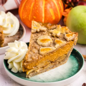 angled shot of slice of pumpkin apple pie on plate with whipped cream