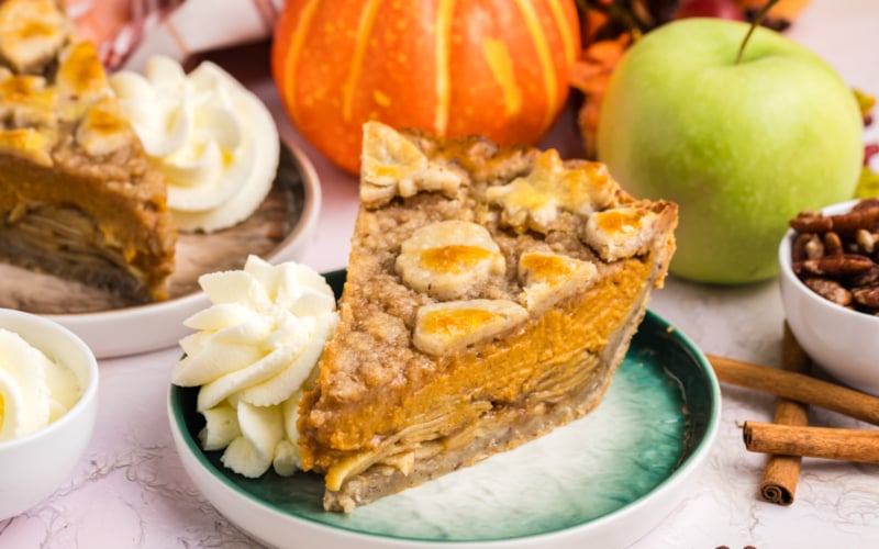 angled shot of slice of pumpkin apple pie on plate with whipped cream