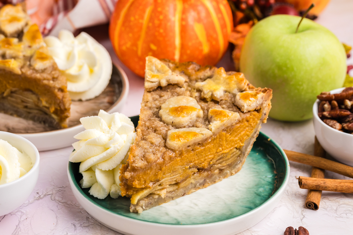 angled shot of slice of pumpkin apple pie on plate with whipped cream