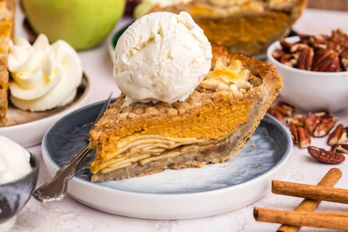 straight on shot of slice of pumpkin apple pie on plate topped with vanilla ice cream