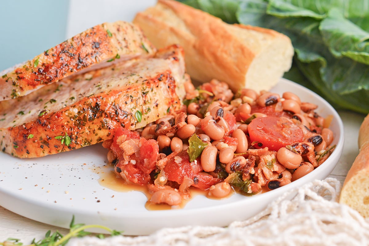 angled shot of black eyed peas on plate with pork and bread