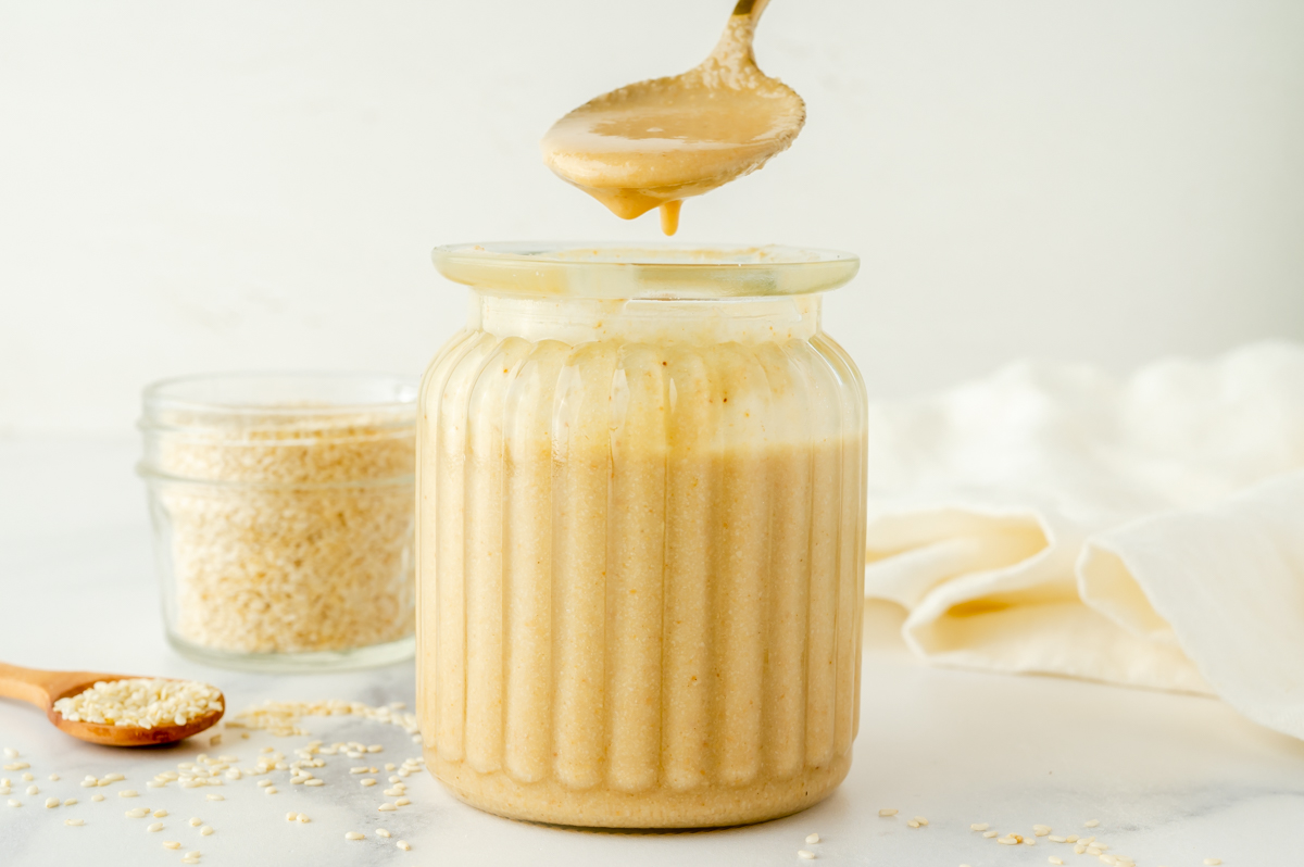 straight on shot of homemade tahini dripping off of spoon into jar