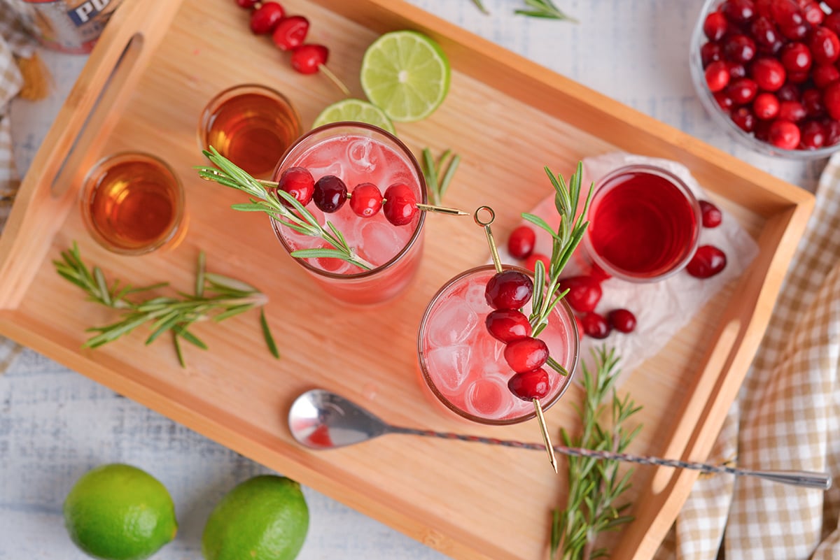 overhead shot of cranberry whiskey sour cocktails on tray with rosemary and cranberries