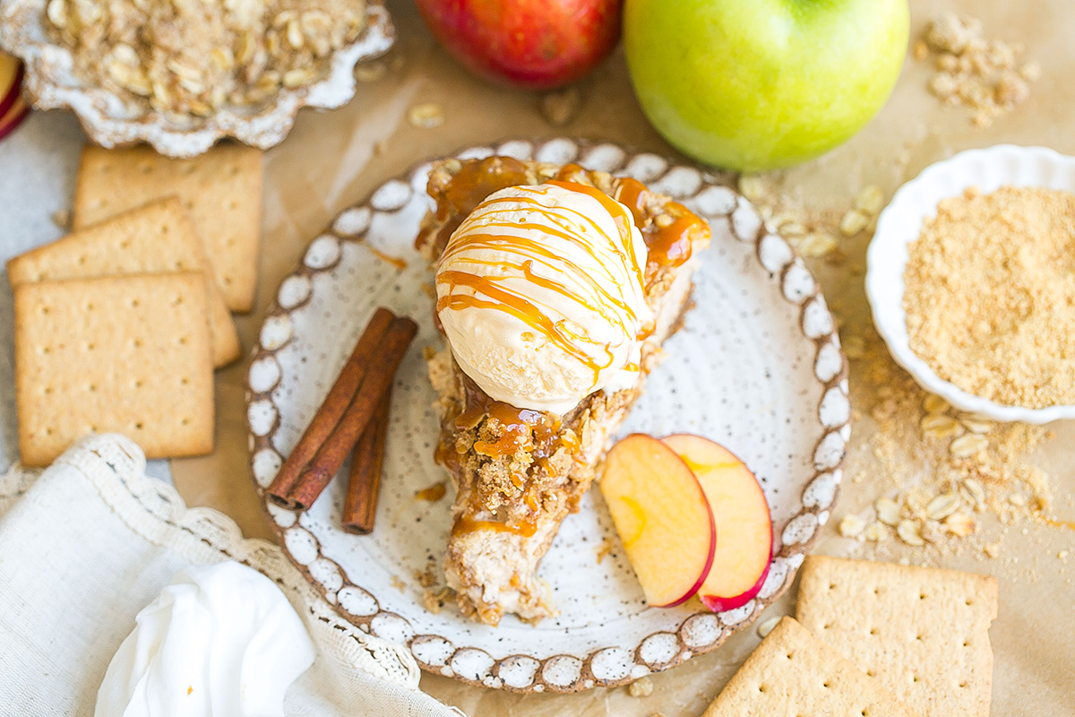 angled shot of slice of apple pie cheesecake topped with scoop of ice cream