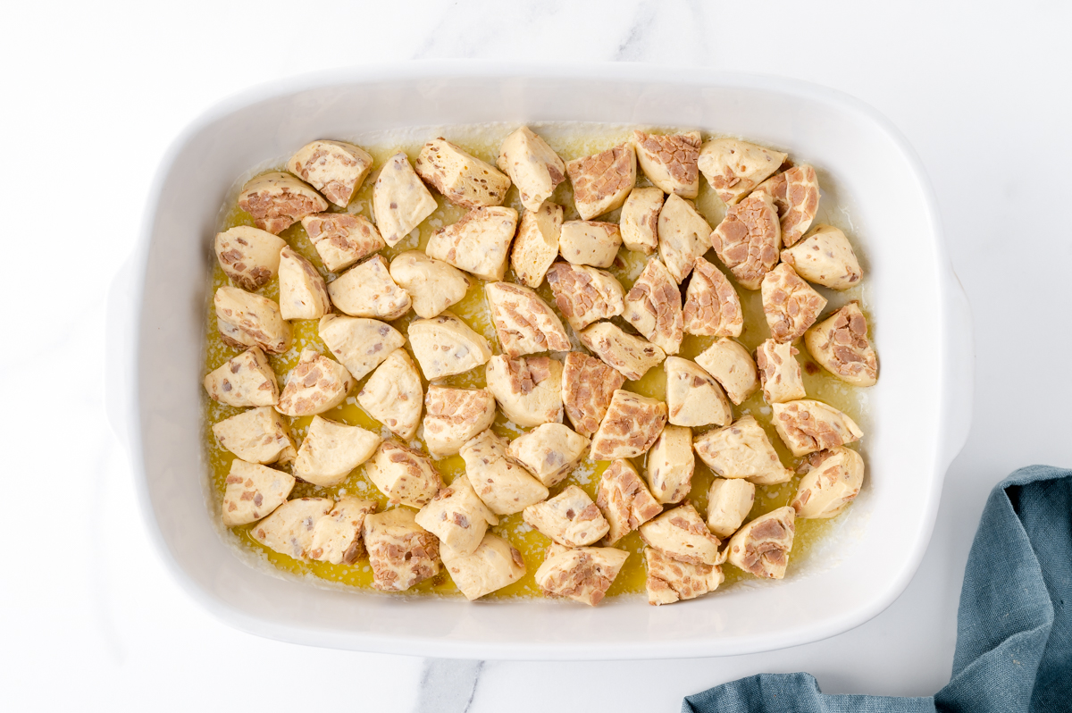 cut raw cinnamon rolls in baking dish with melted butter