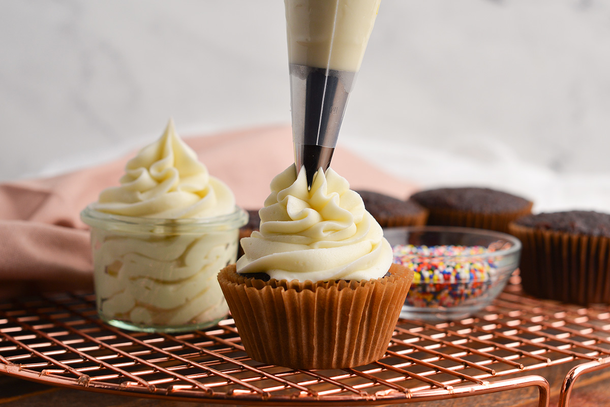 piping frosting onto a chocolate cupcake