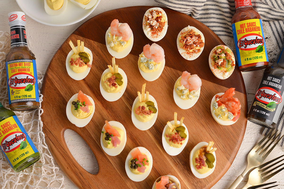 overhead shot of deviled egg flight on wood board with hot sauce bottles