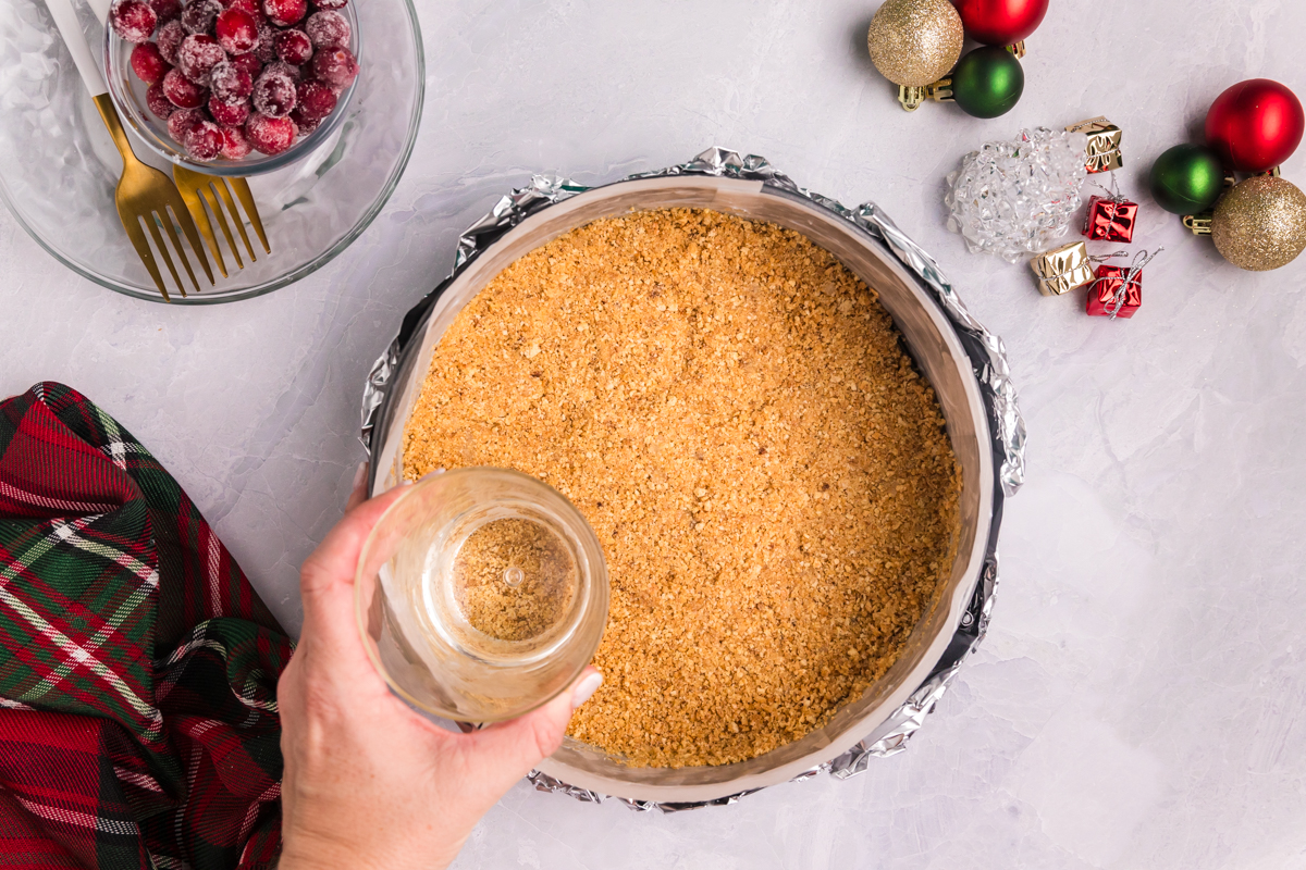 glass pressing graham cracker crust into springform pan