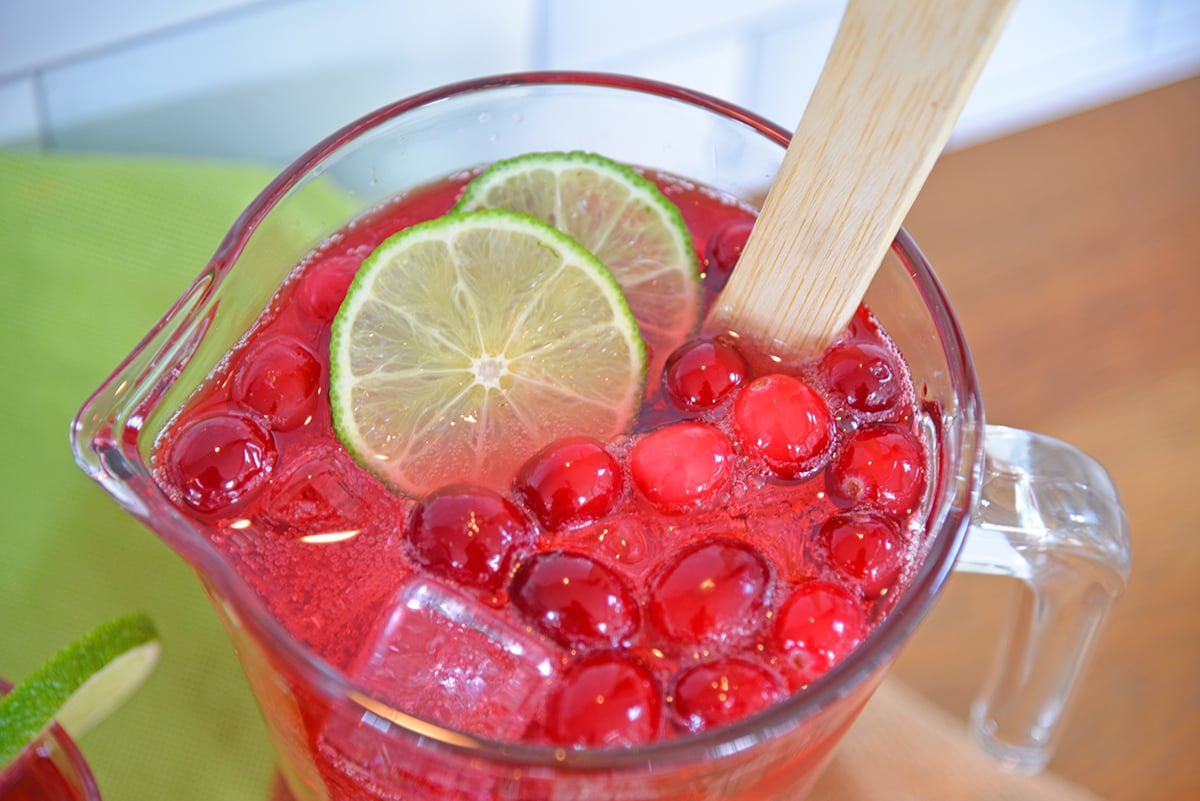 Pitcher of holiday cranberry punch with lime and fresh cranberries with a wood spoon