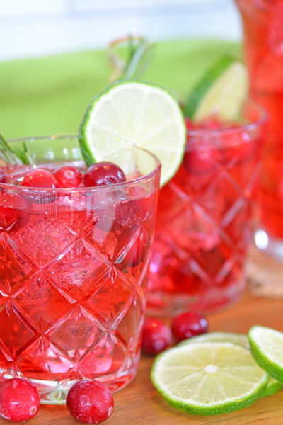 Side view of cocktail glass with cranberries, ice cubes and lime