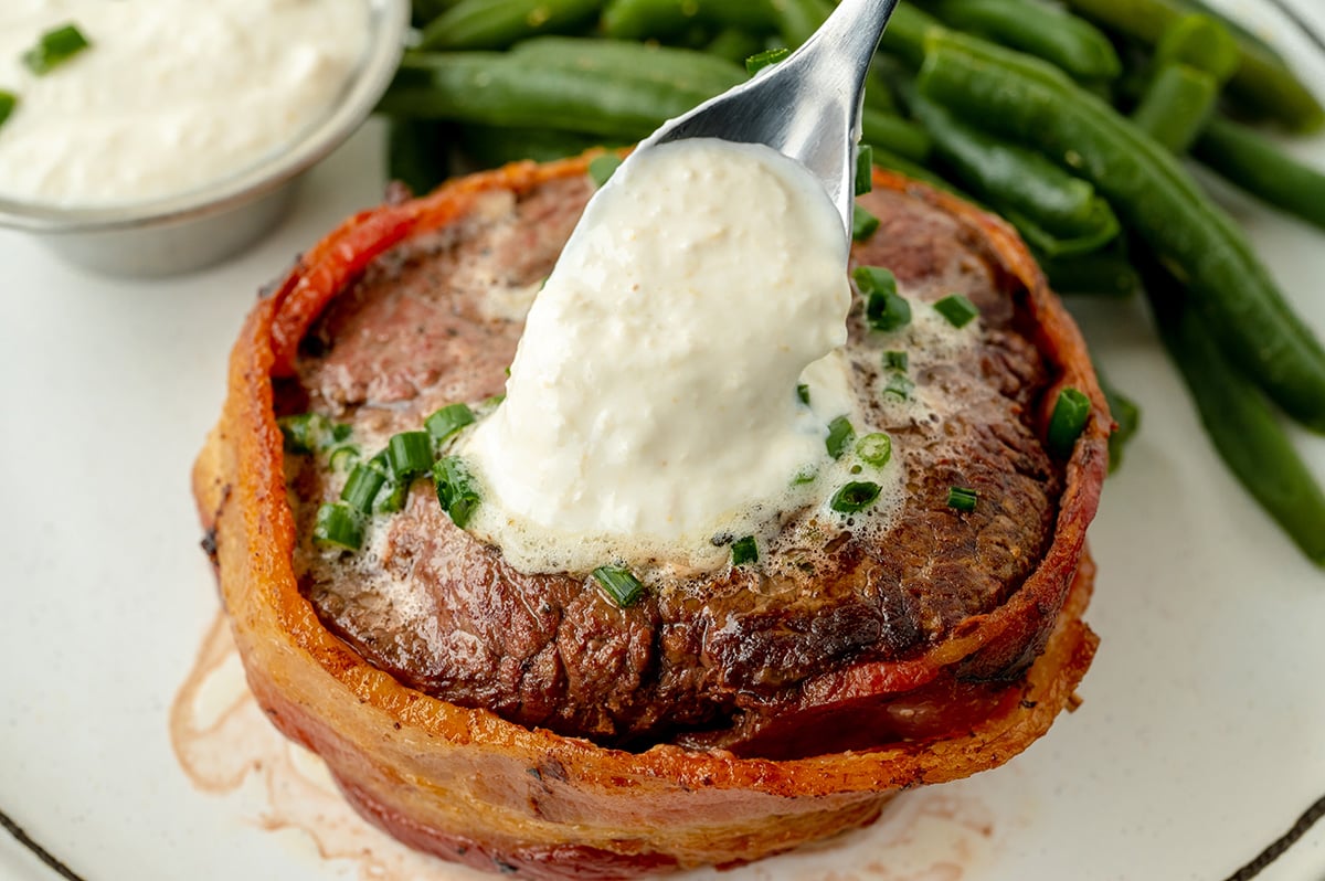 angled shot of spoon adding creamy horseradish sauce to steak