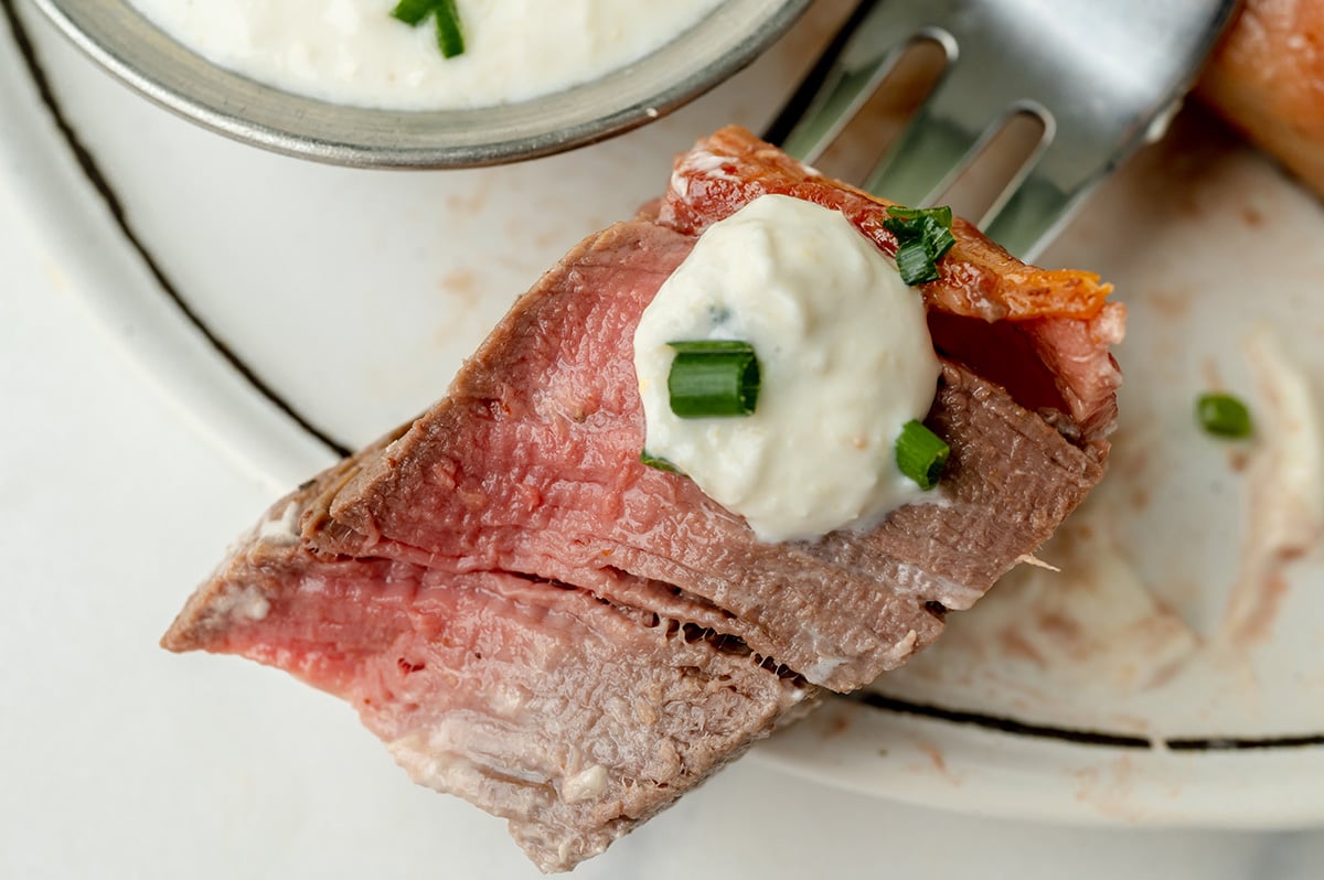 close up of bite of steak on fork topped with sauce