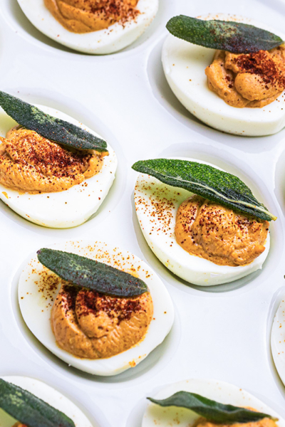 angled shot of platter of deviled eggs topped with sage leaves