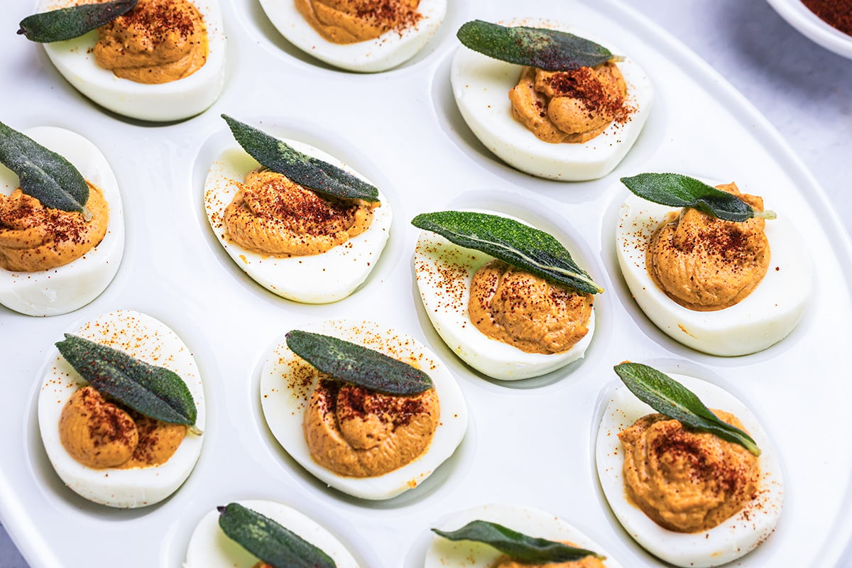 angled shot of platter of deviled eggs topped with sage leaves