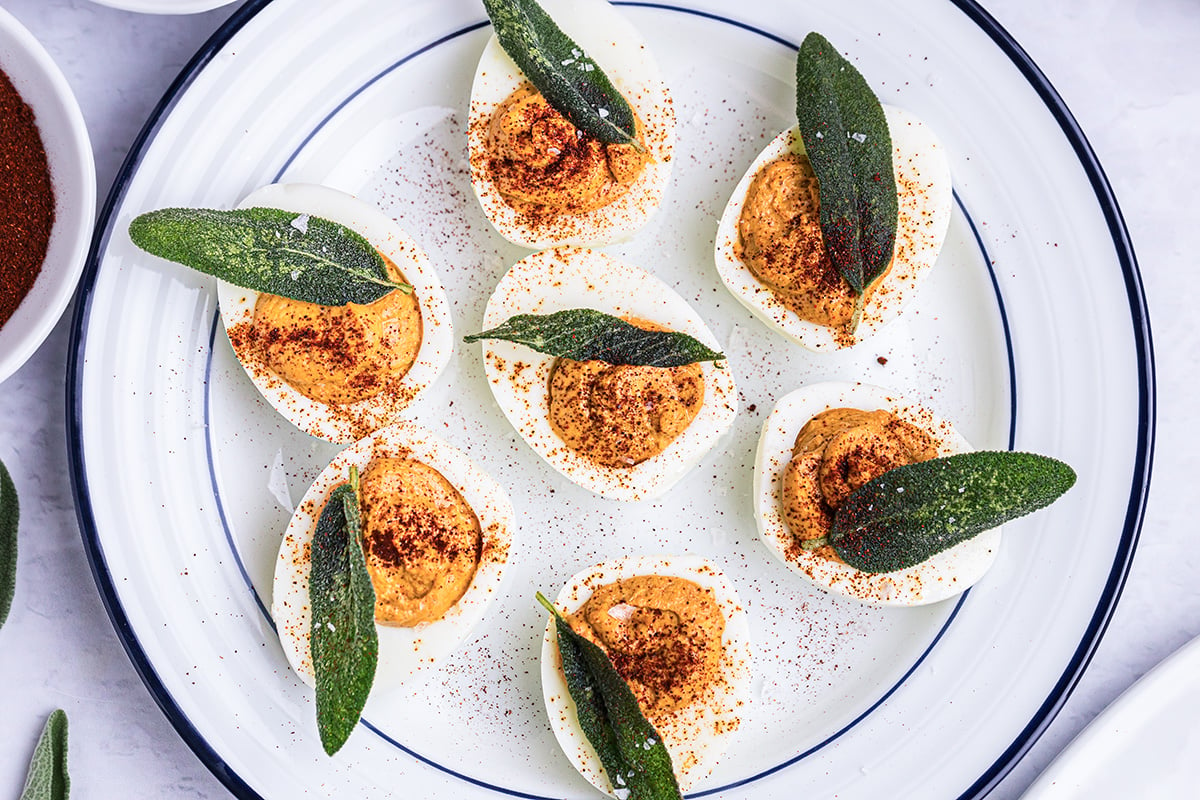 deviled eggs topped with sage leaves on plate