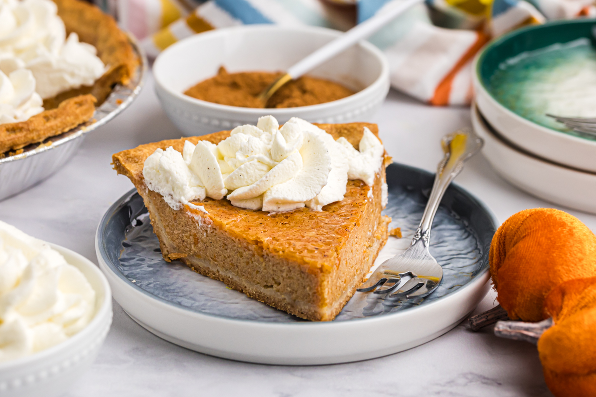 angled shot of slice of sweet potato pie topped with whipped cream on plate