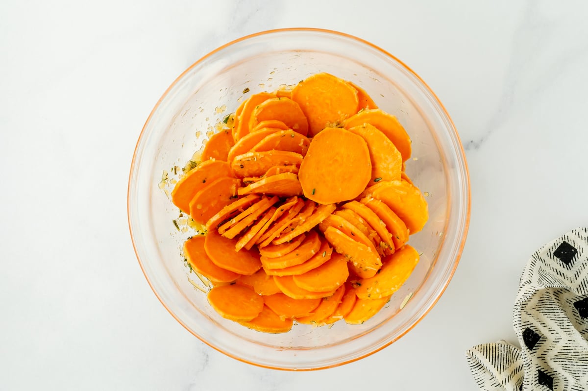 sliced sweet potatoes in bowl with seasonings