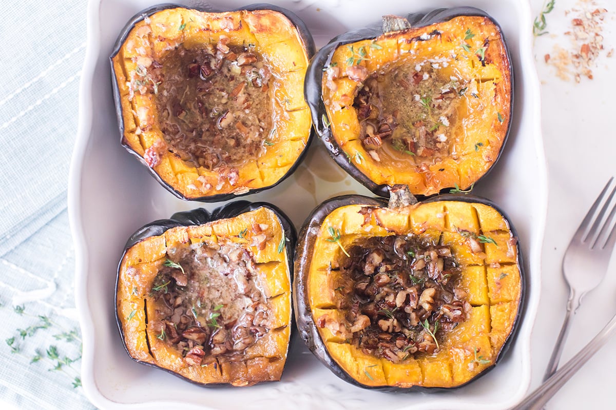 overhead shot of four pecan thyme acorn squash halves in baking dish