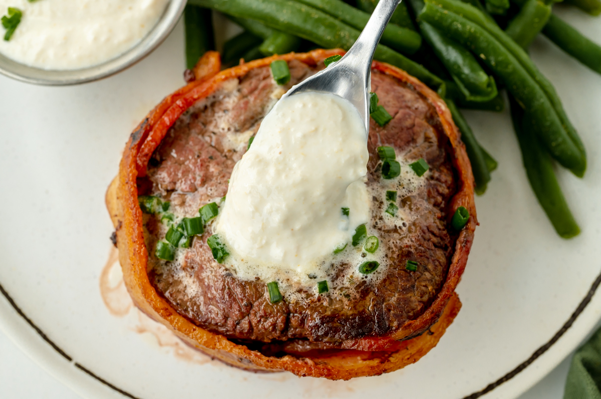 spoon adding horseradish sauce to bacon wrapped filet mignon