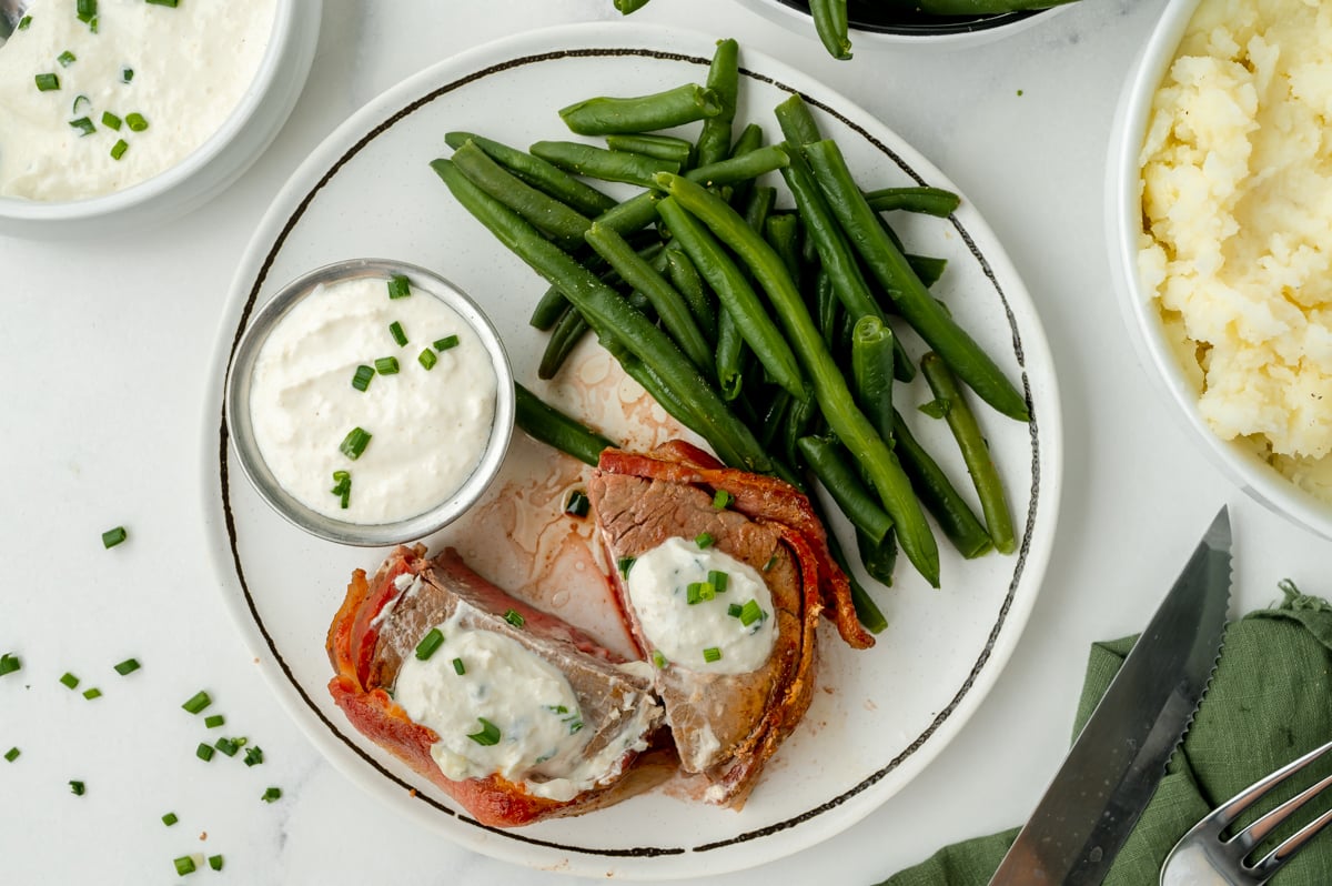 overhead shot of bacon wrapped filet mignon cut in half on plate with green beans and horseradish sauce