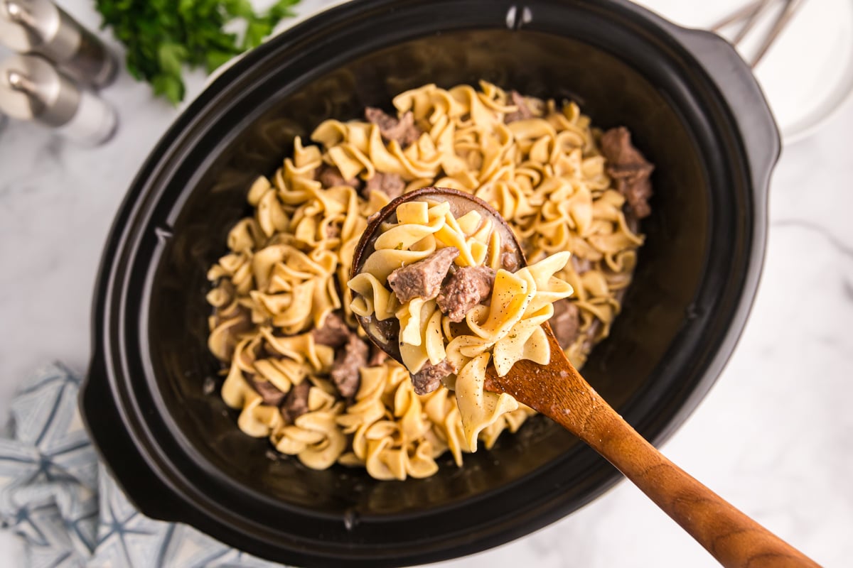 overhead shot of ladle in beef and noodles in crock pot