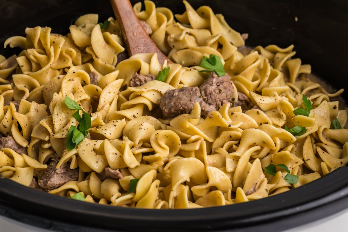 angled shot of ladle in crock pot of beef and noodles