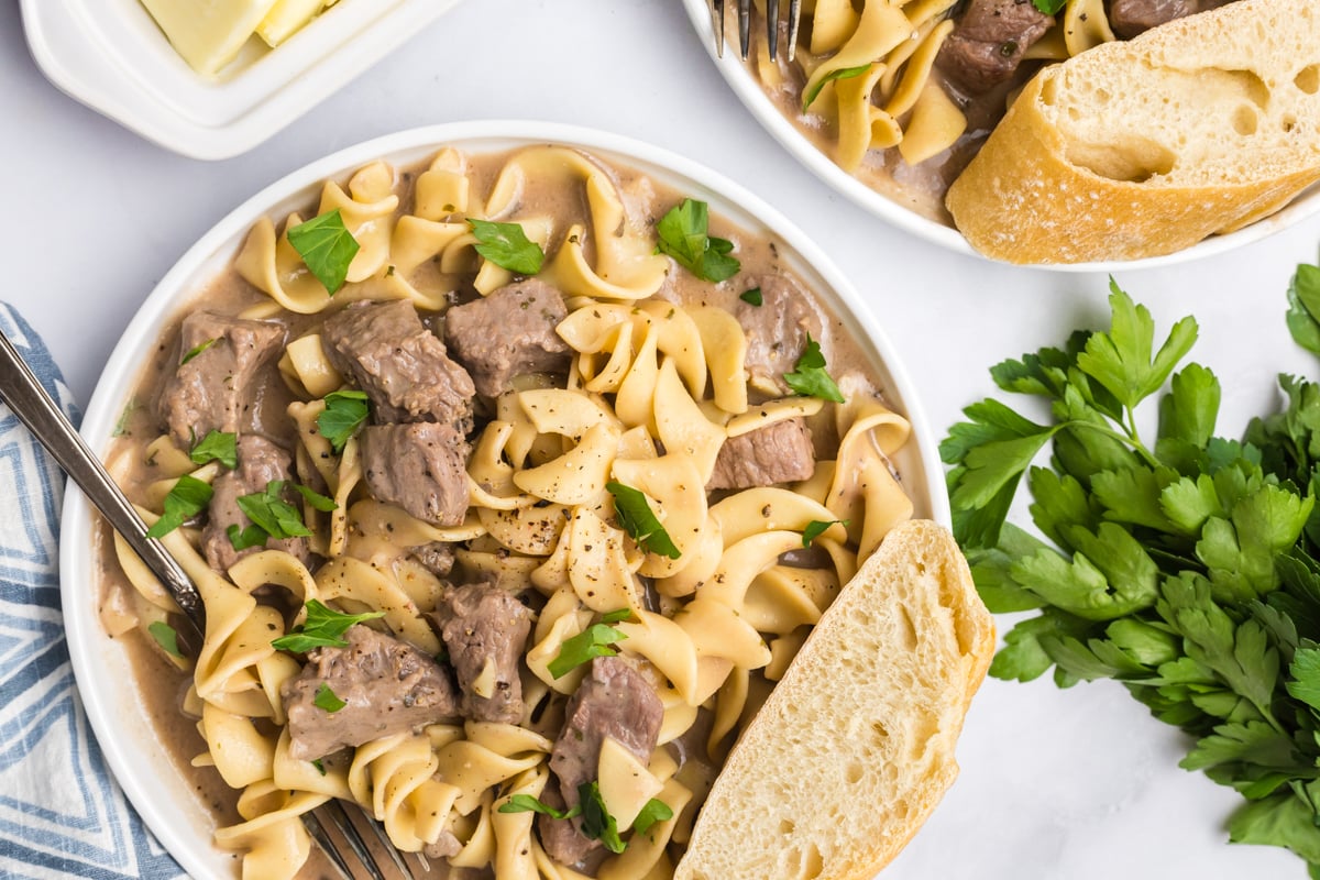 close up overhead shot of fork in plate of crock pot beef and noodles with crusty bread