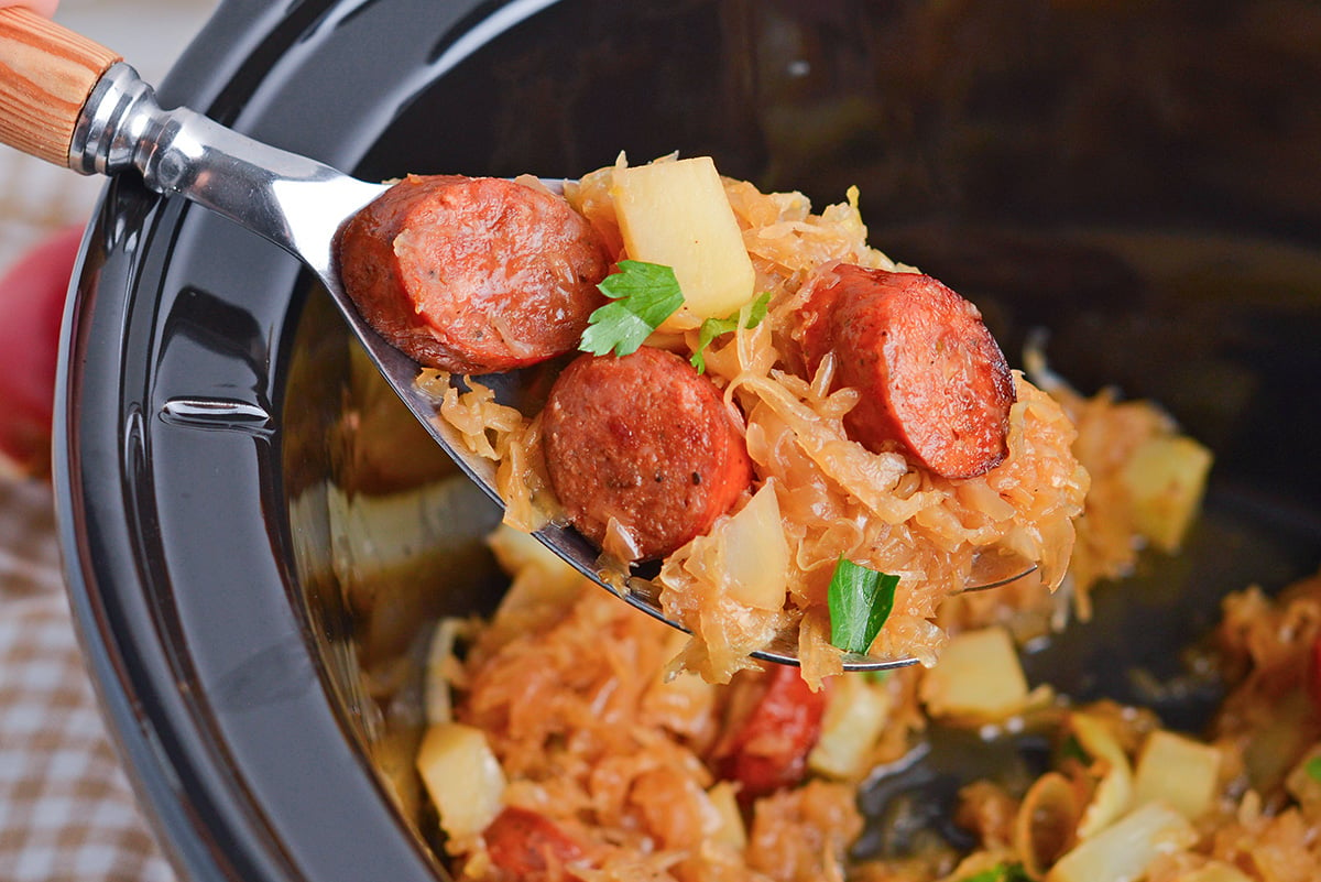 close up of crock pot kielbasa and sauerkraut on a serving spoon