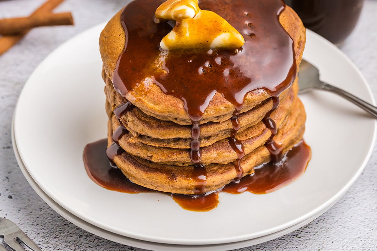 close up angled shot of syrup dripping over stack of stack of gingerbread pancakes