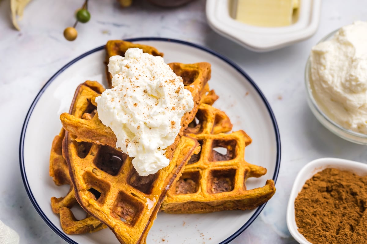 overhead shot of whipped cream on stack of pumpkin waffles